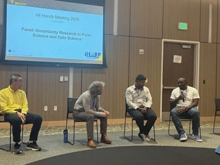 Four panelists seated at the front of the meeting room, one speaking into a handheld microphone, beneath a projected slide reading Panel: Uncertainty Research in Polar Science and Data Science, All Hands Meeting 2026.